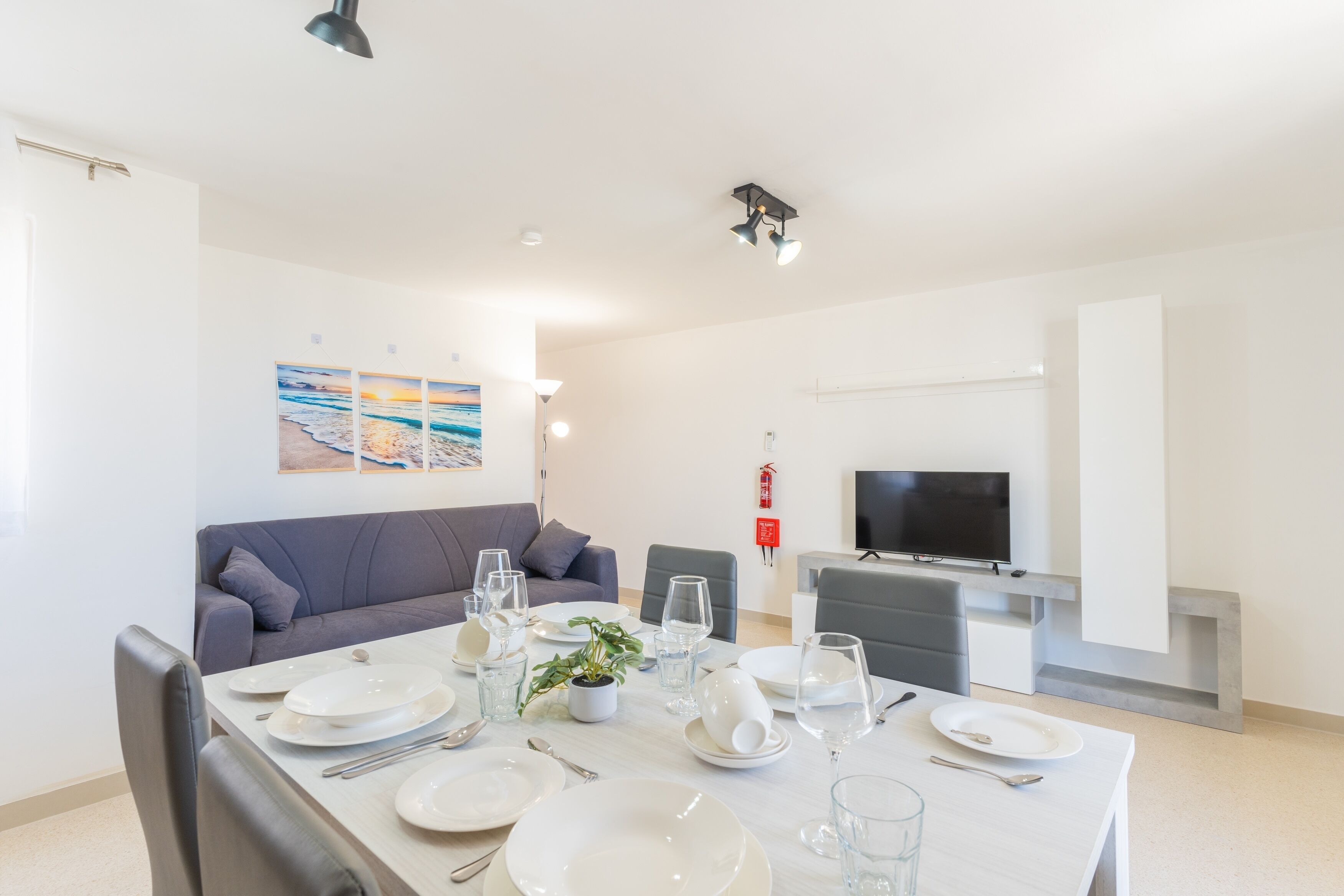 A modern dining area with a table set for four, a sofa, a flat-screen TV, and a fireplace.