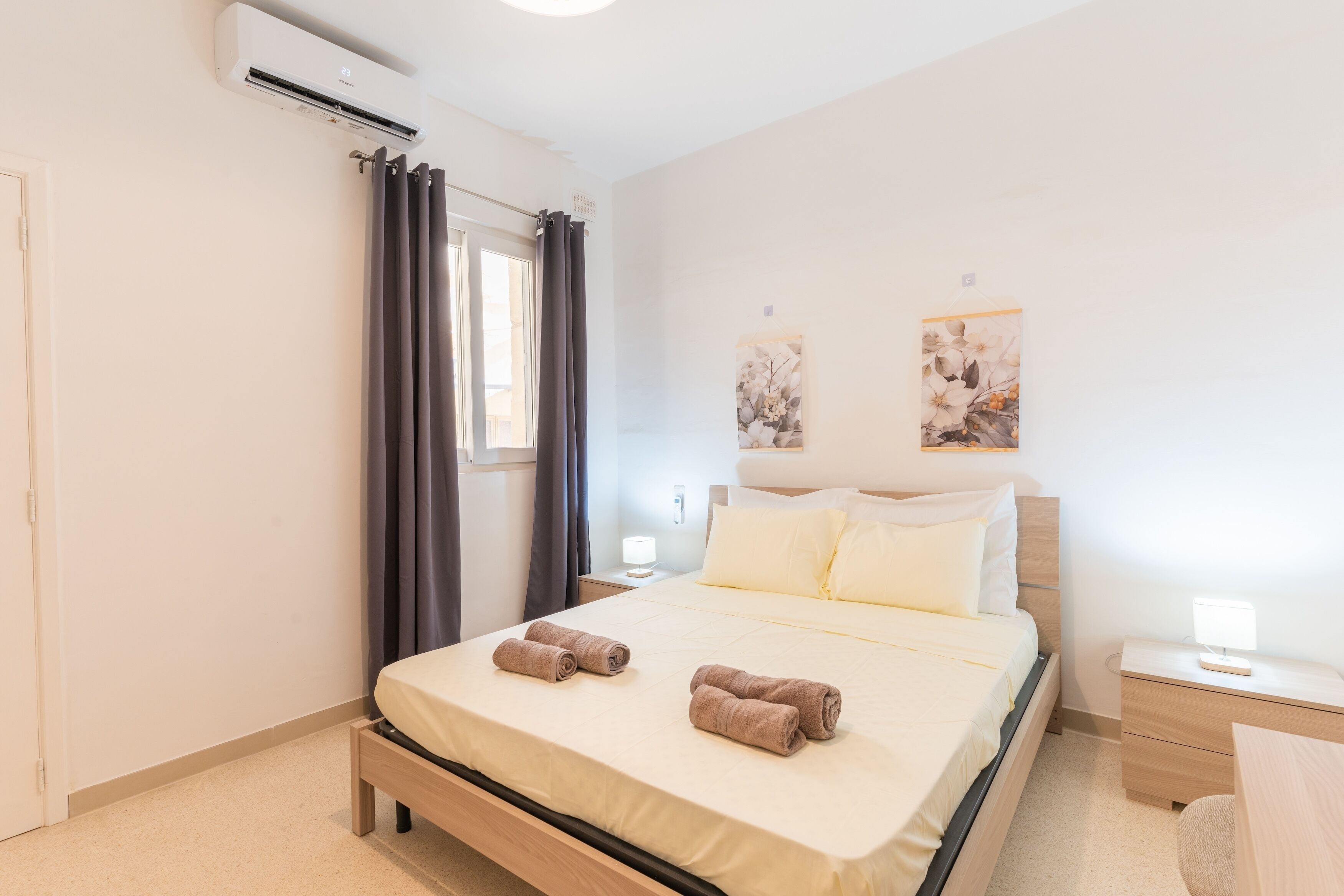 Una camera da letto ordinata con un letto, comodini e un condizionatore d'aria a parete.