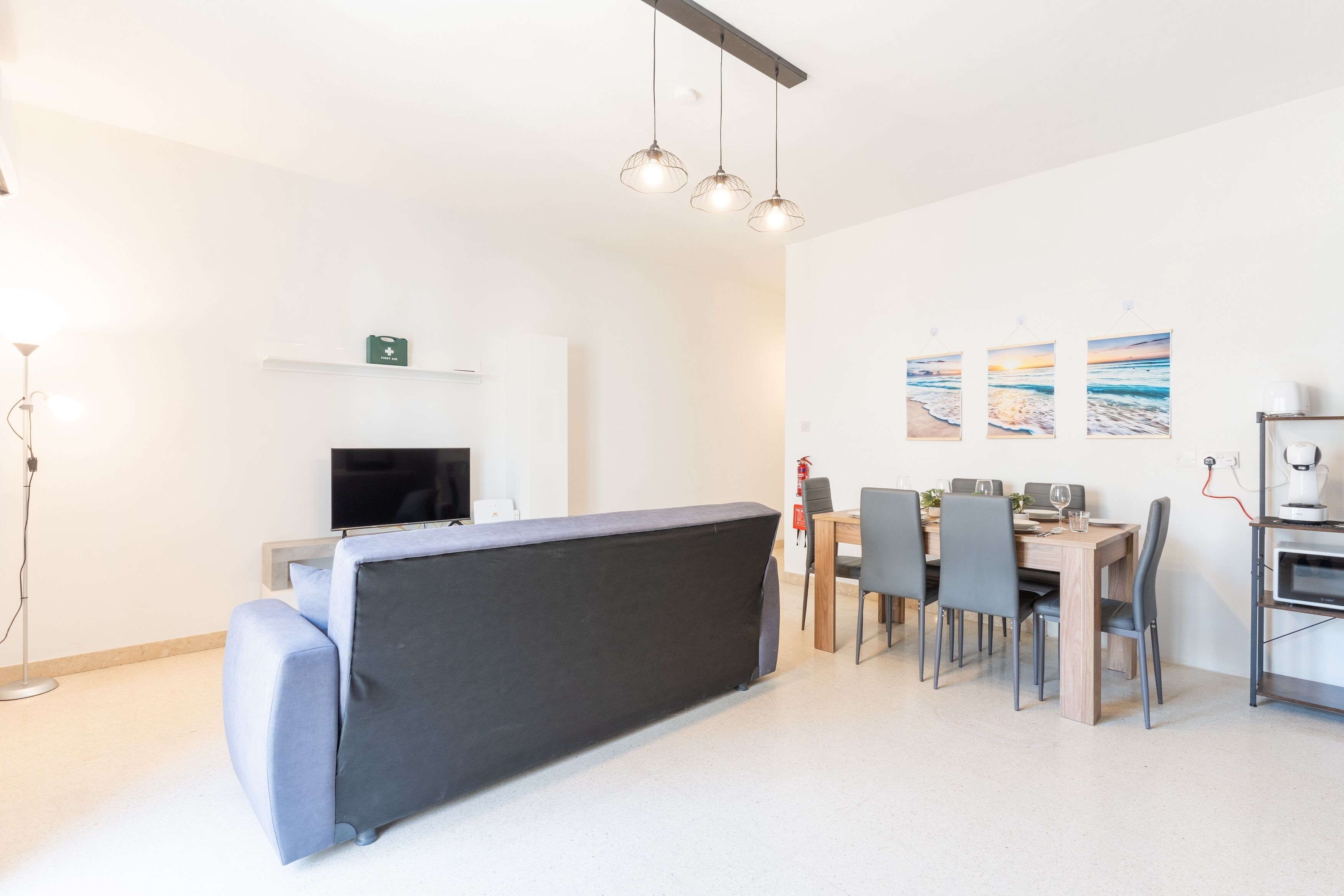 Een moderne woonkamer met een bank, een eettafel, stoelen, een televisie en kunstwerken aan de muur.