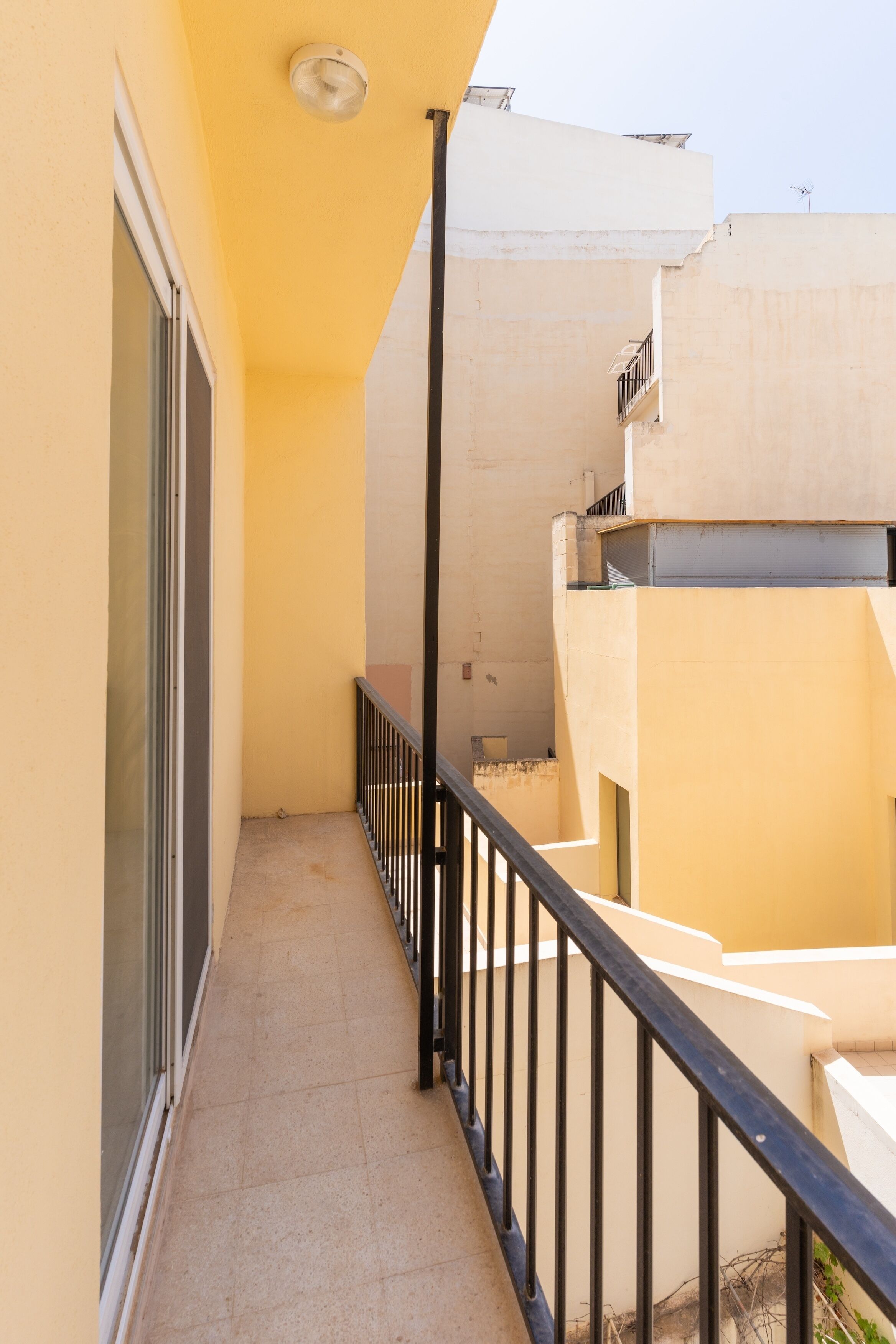Een smal balkon met een zwart hekwerk, een glazen deur en een betonnen vloer.