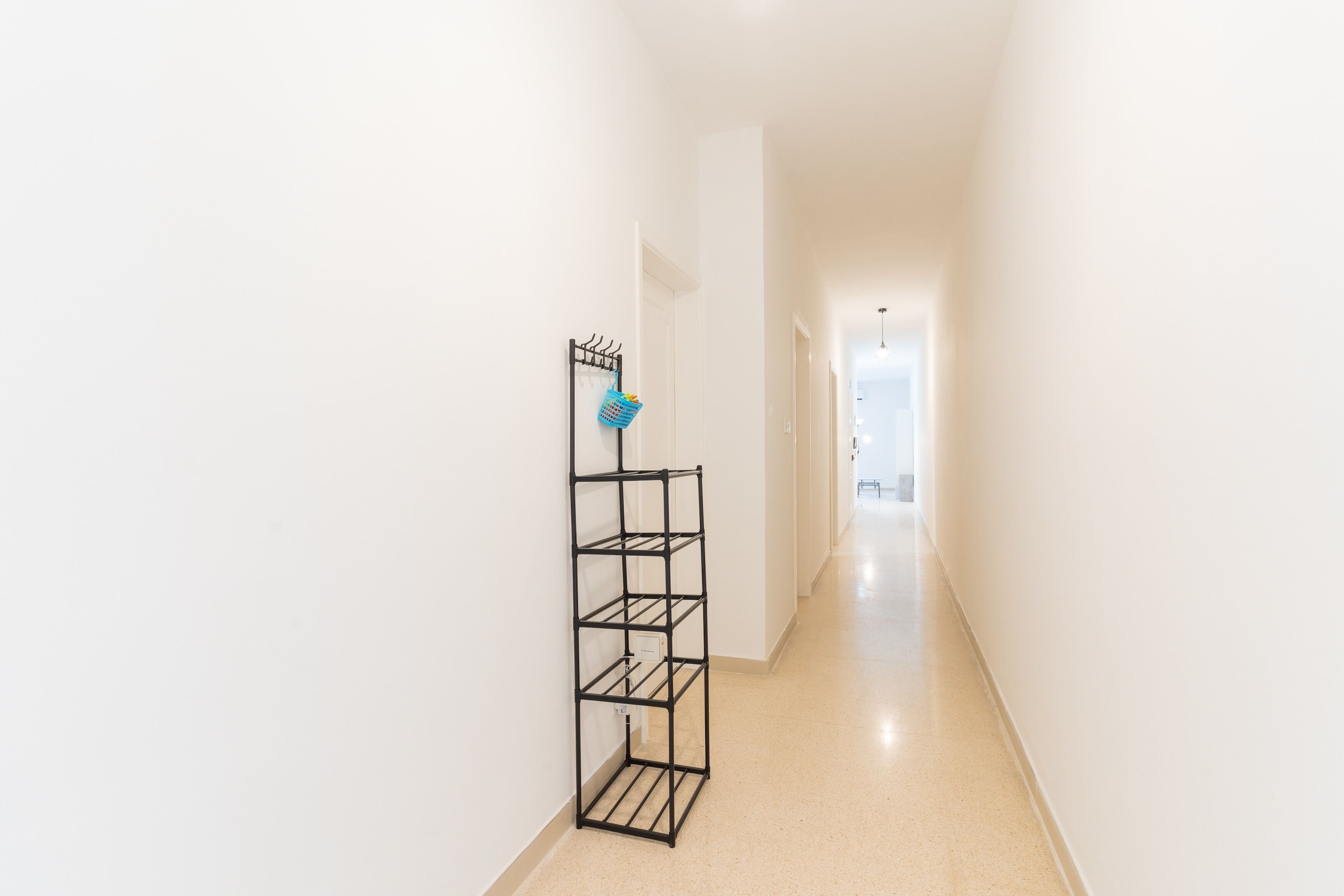 Un couloir avec une étagère en métal noir adossée au mur, une porte blanche au fond et un plancher de couleur claire.