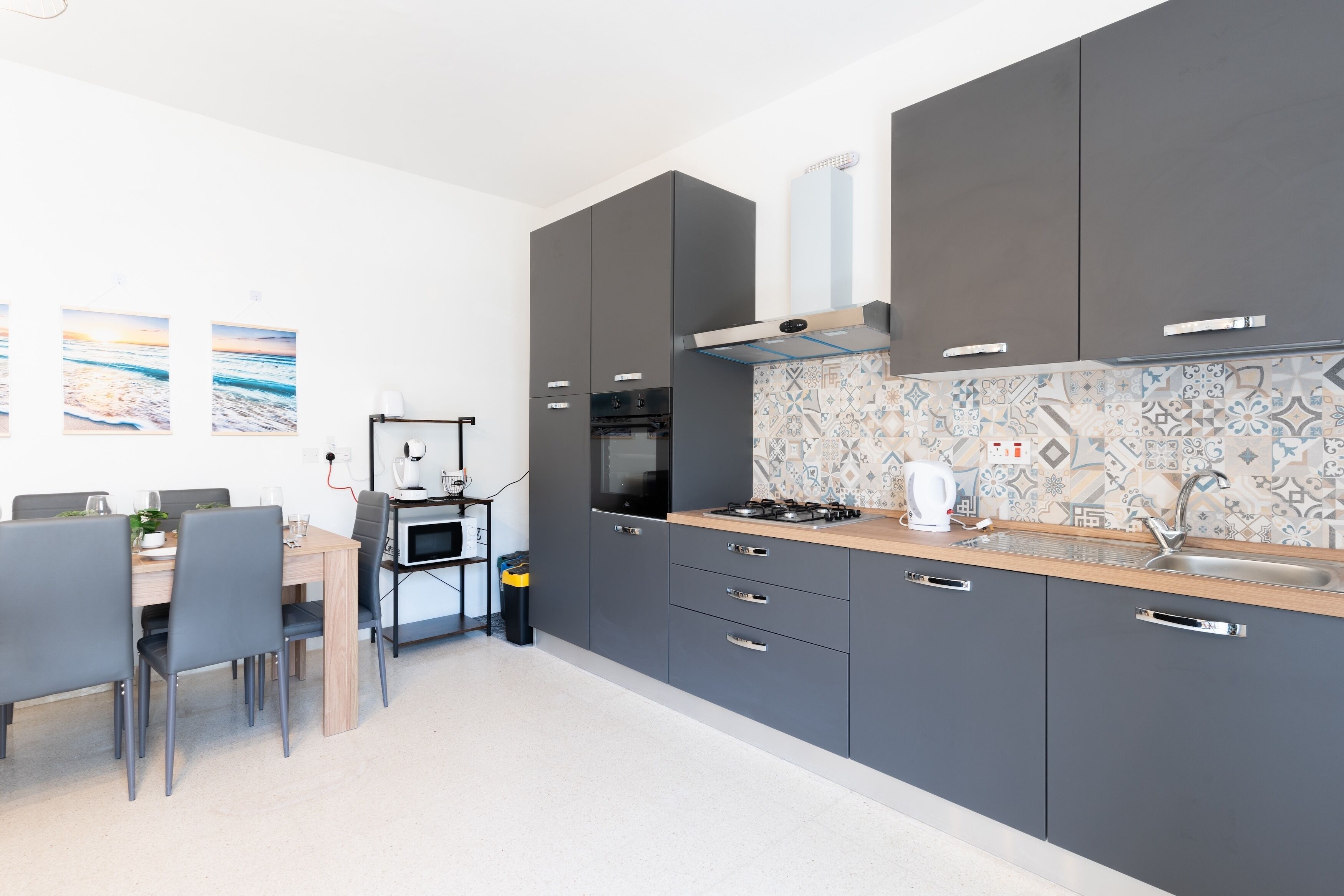 Una cucina moderna con mobili grigi, un piano di lavoro in legno e uno schienale piastrellato.