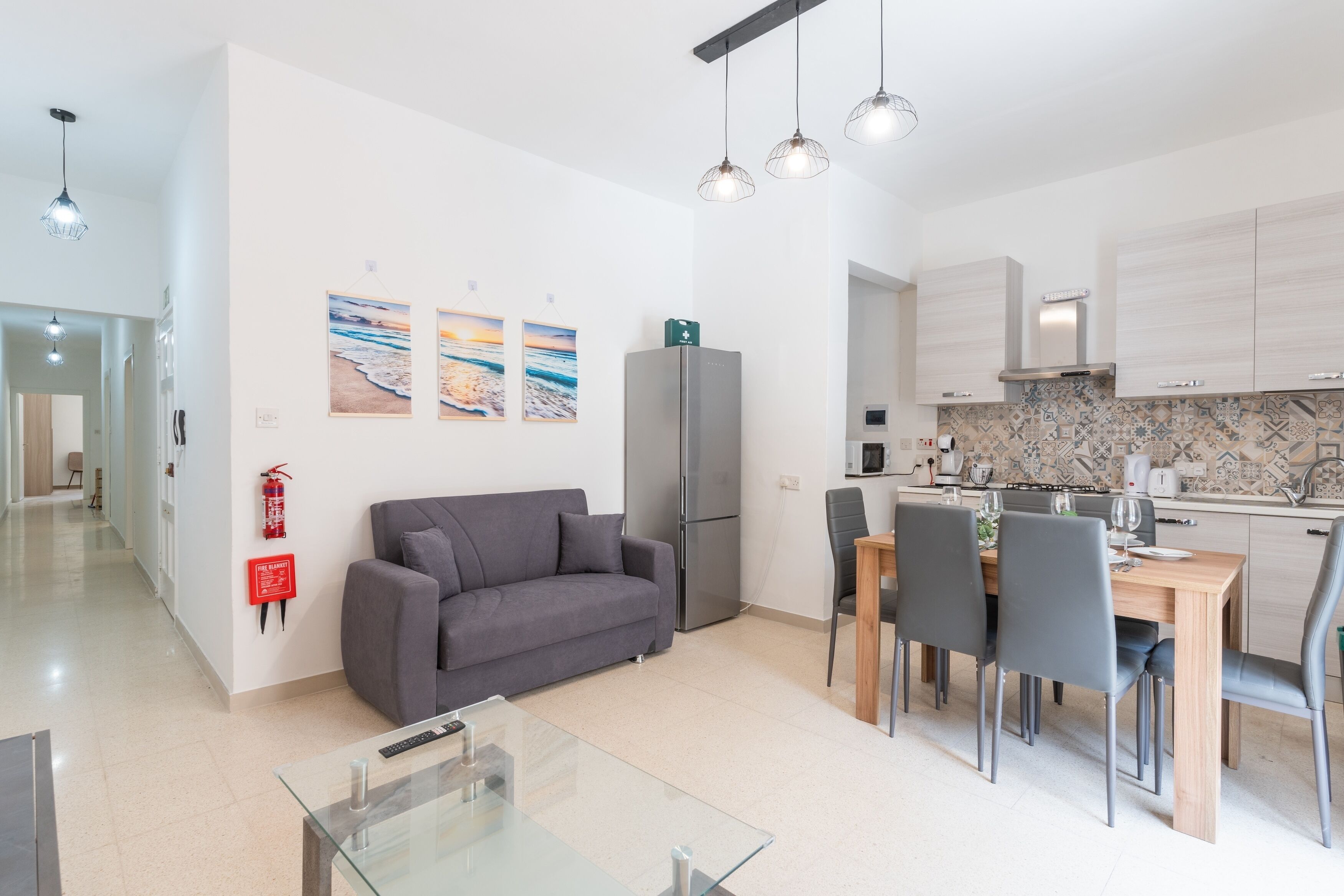 A modern kitchen with a dining area, a grey sofa, and a glass coffee table.