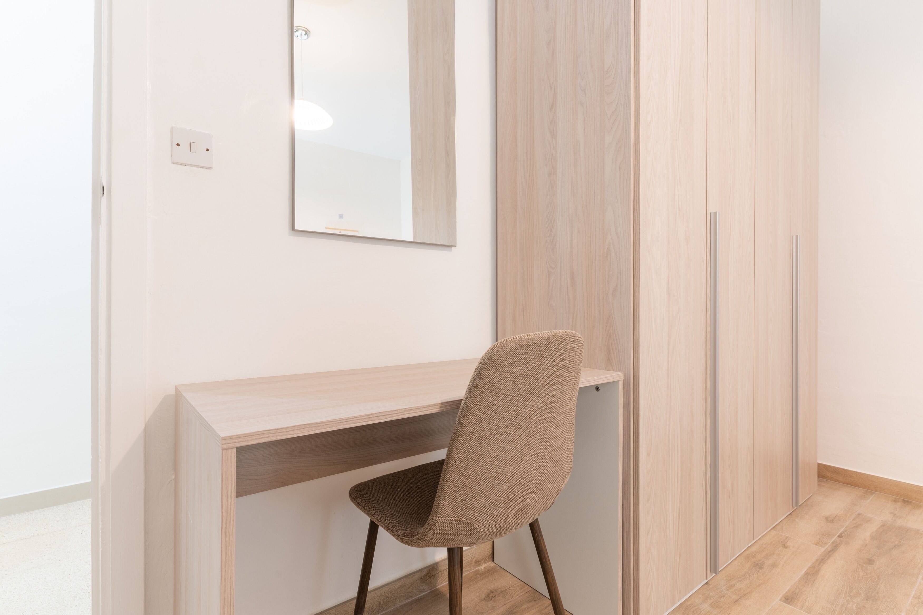 A modern room with a wooden desk, a brown woven chair, and a wardrobe with vertical handles.
