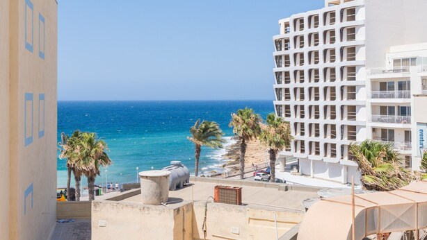 A coastal hotel with a view of the sea, palm trees, and a modern building with balconies. - Tempo Suites (St. Paul's Bay)