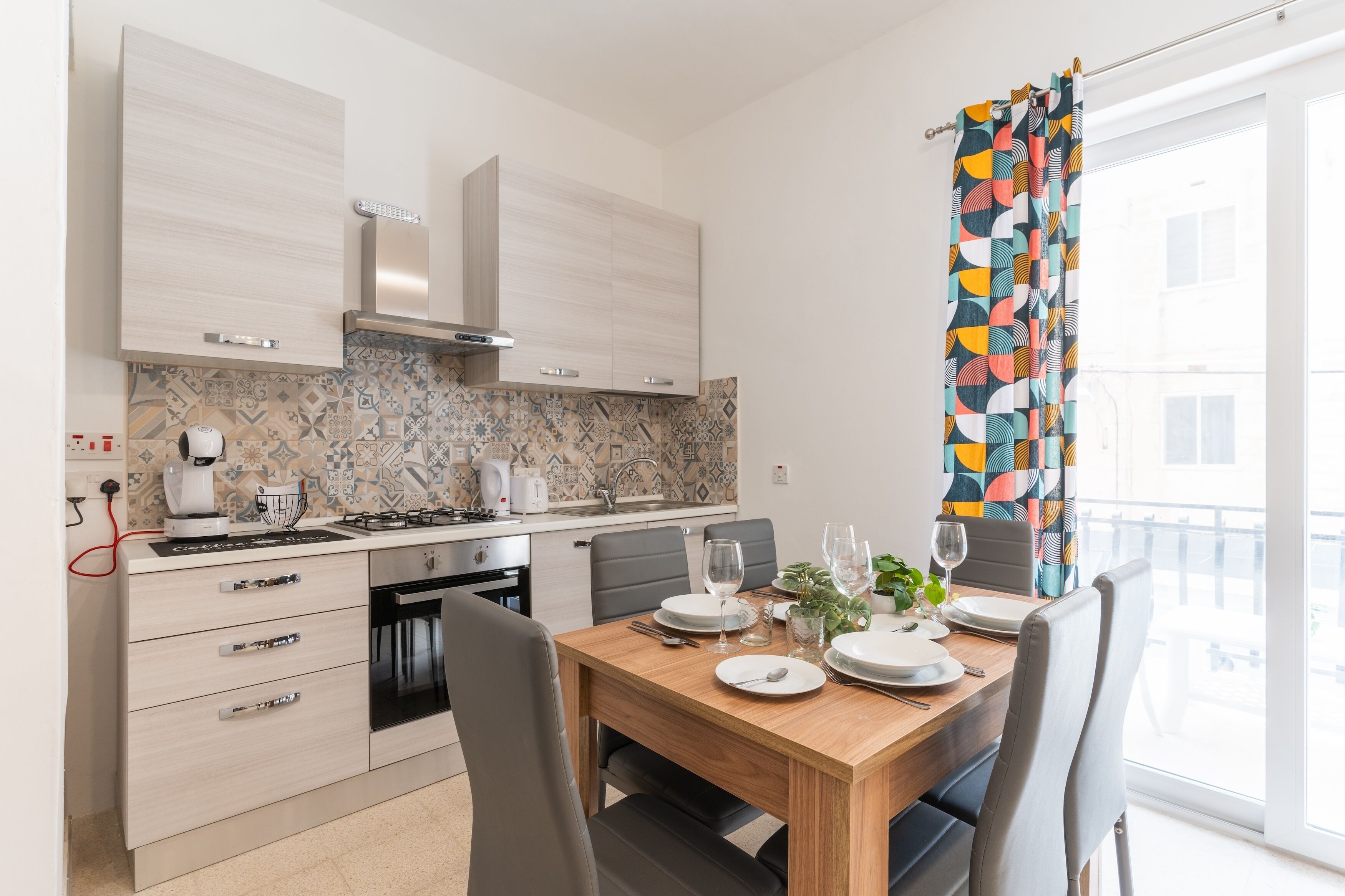 Ett modernt kök med matplats, med kakel som stänkskydd, en inbyggd ugn och ett matbord med plats för fyra personer.