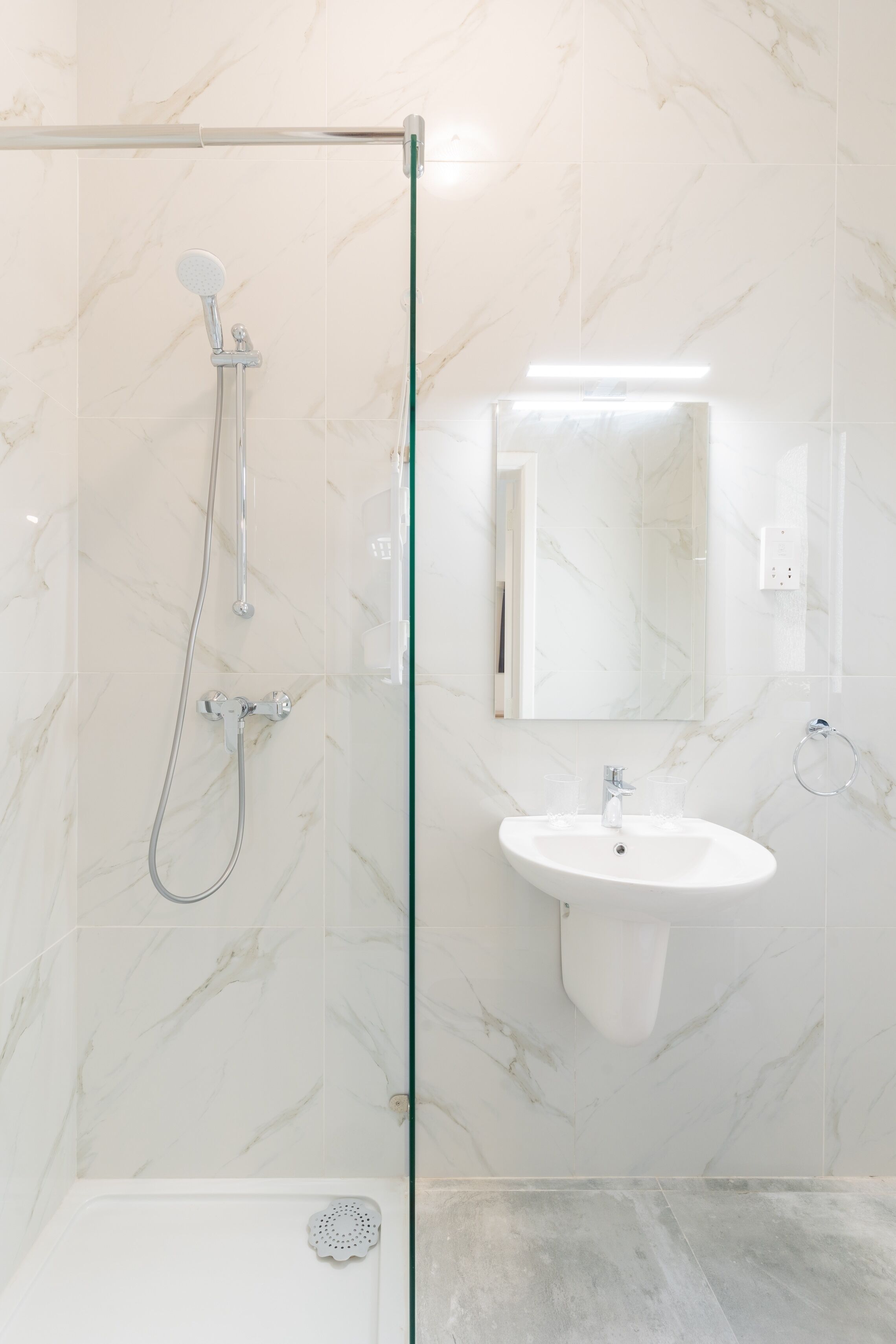 A modern bathroom with a glass shower enclosure, a white sink, and a marble-tiled wall.