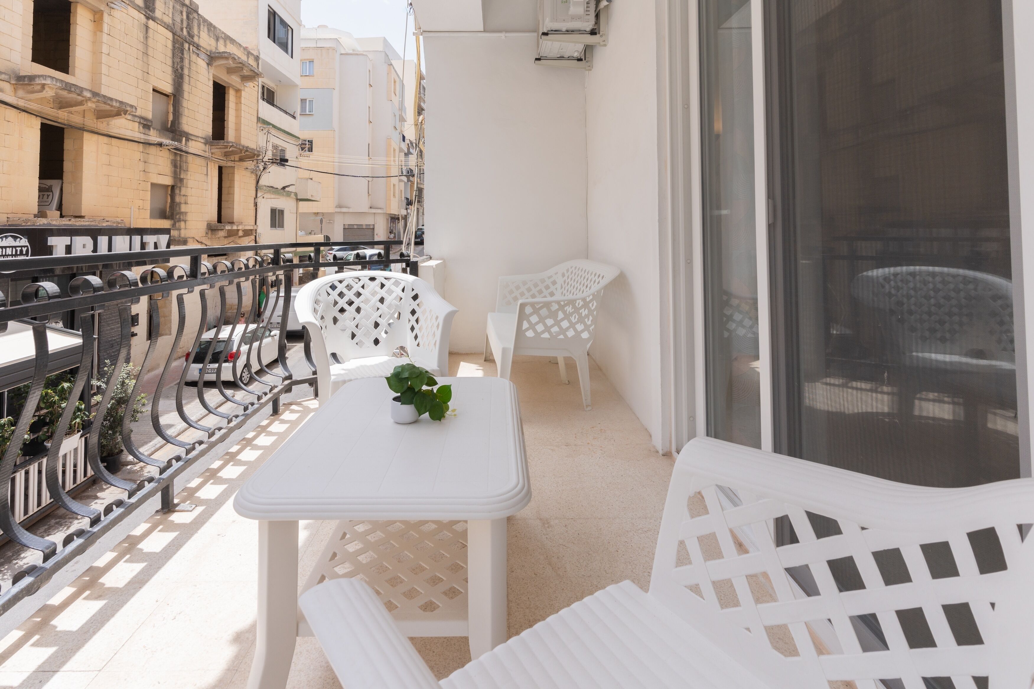 Ein Balkon mit weißen Möbeln, darunter ein Tisch und Stühle, sowie ein Blumentopf.