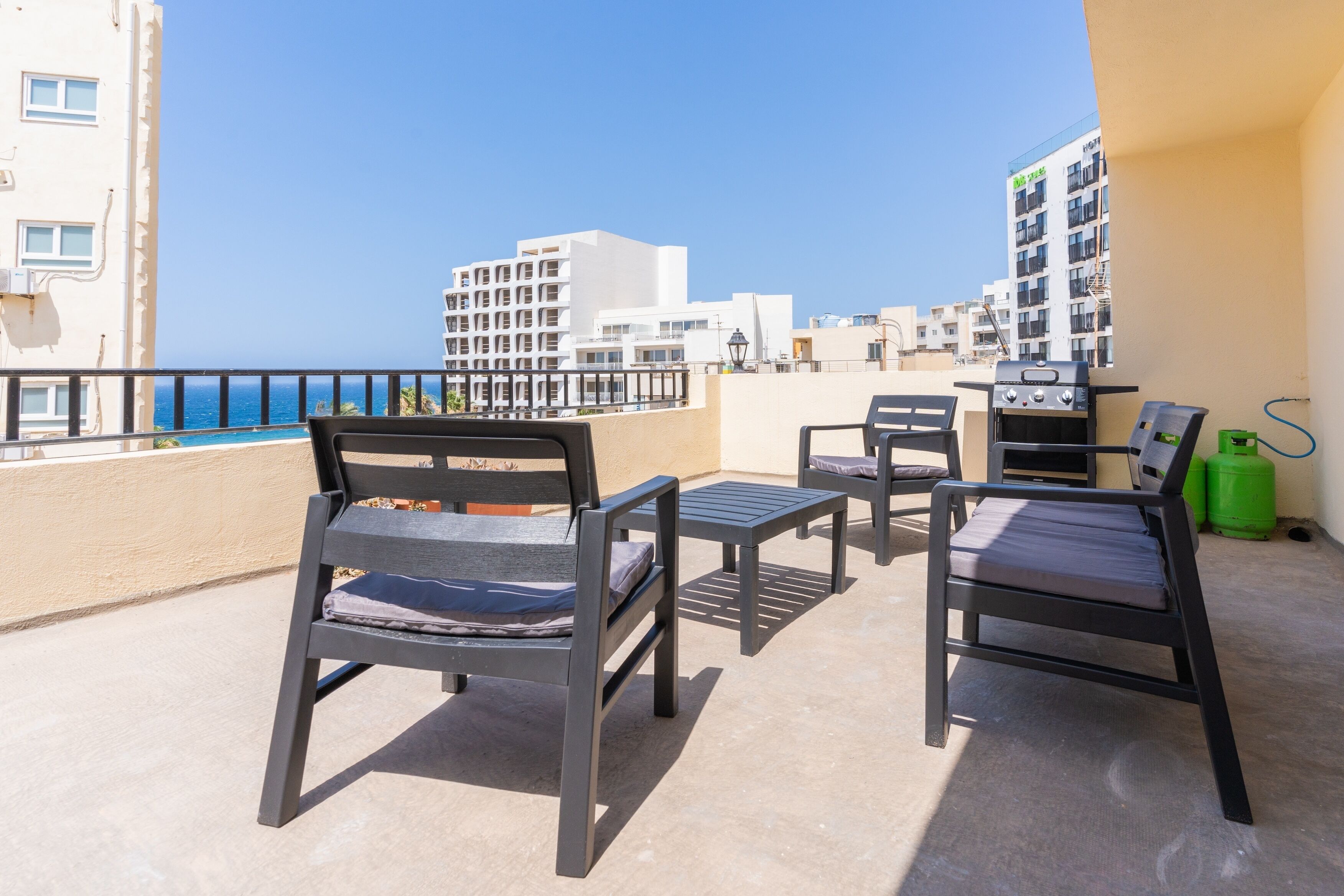 A balcony with two chairs and a table, overlooking a clear blue sea and buildings in the background.