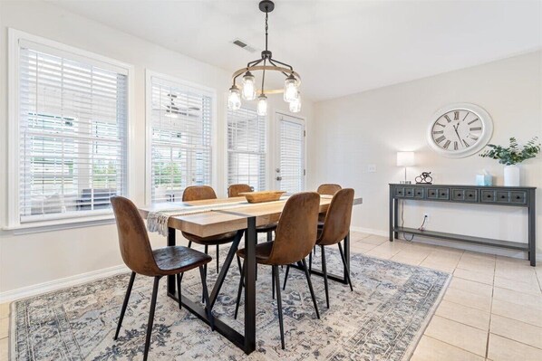Un coin repas comprenant une table en bois, six chaises, un lustre, une horloge et une console ornée d’objets décoratifs.