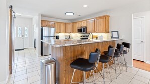 A modern kitchen with wooden cabinets, stainless steel appliances, and a bar area with black chairs.