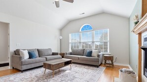 A living room with two sofas, a coffee table, a fireplace, and a large window with blinds.
