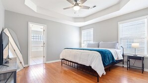 A bedroom with a bed, a desk, a ceiling fan, and a door.
