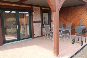 A covered patio with a brick wall, sliding glass doors, and a grill station. - Modern Holiday Home in Brusow With Roofed Terrace (Kroepelin)