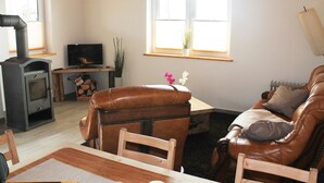 A living room with a fireplace, leather sofa, wooden table, and a television. - Modern Holiday Home in Brusow With Roofed Terrace (Kroepelin)