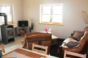 A living room with a fireplace, leather sofa, wooden table, and a television. - Modern Holiday Home in Brusow With Roofed Terrace (Kroepelin)