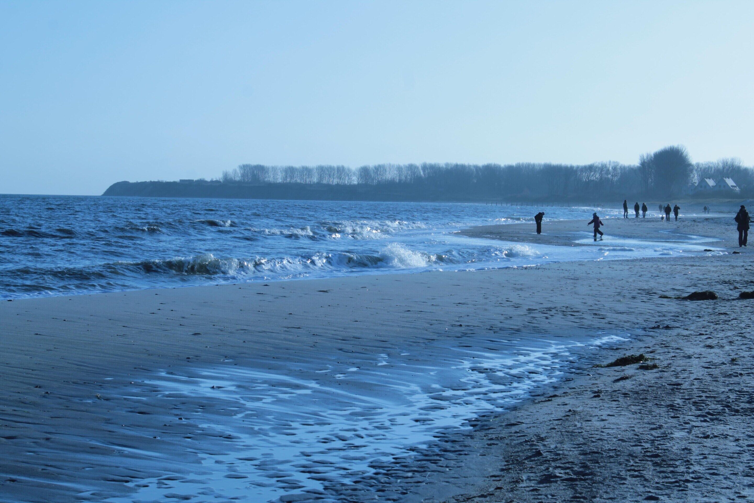 Una playa con gente caminando y jugando en el agua.