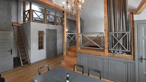 Habitación estilo loft con una mesa de comedor, sillas, una araña y una cama alta con escalera de madera.