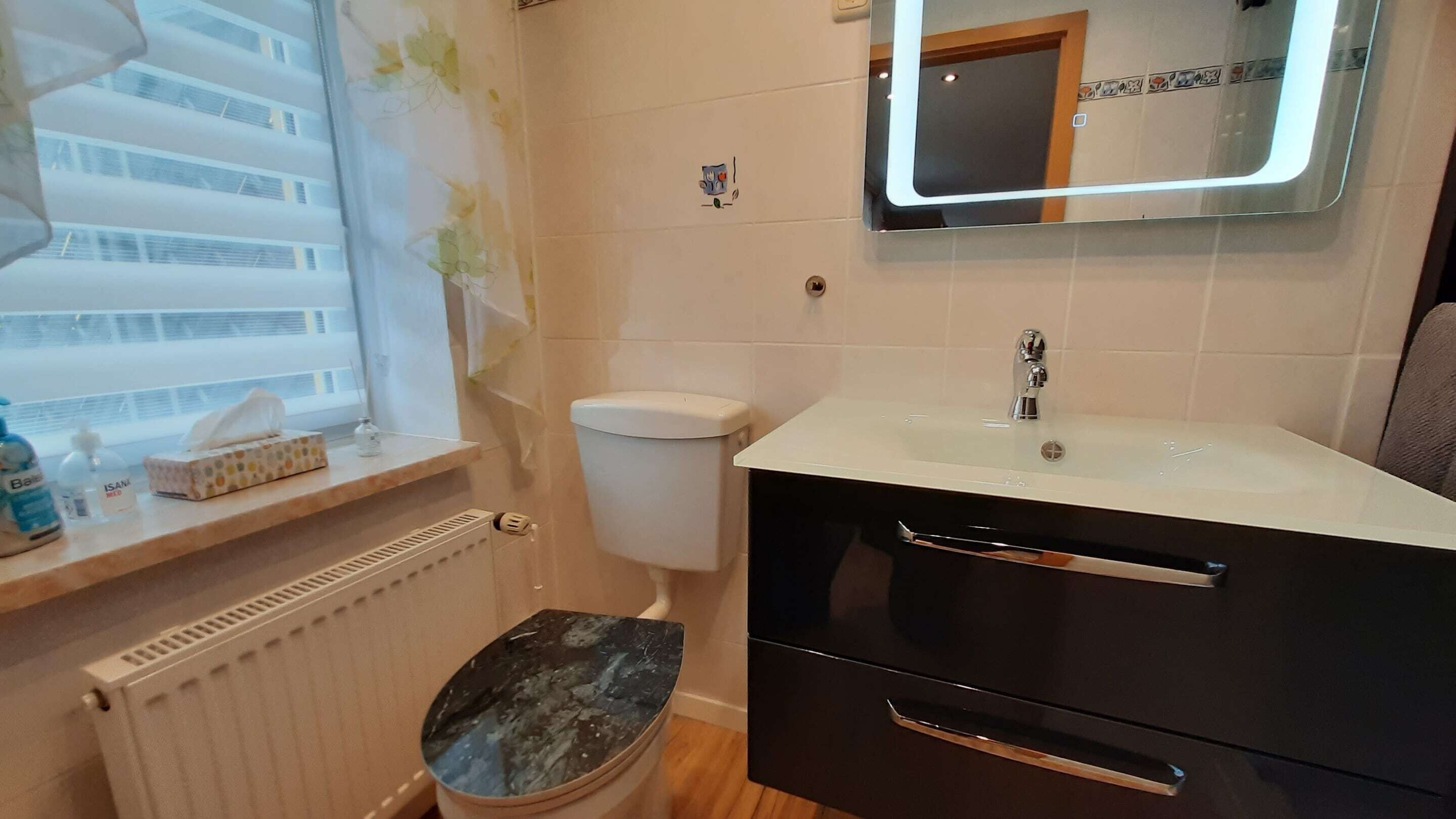 A bathroom with a toilet, a sink, a mirror, and a window with a view of a building.