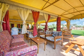 A covered outdoor seating area with patterned sofas, wooden tables, and chairs. - Holiday Home in Castiglione del With Pool (Castiglione del Lago)