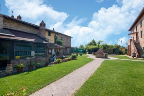 A courtyard with a paved walkway, a brick building with a shop on the left, and a staircase leading to a second floor on the right. - Holiday Home in Castiglione del With Pool (Castiglione del Lago)