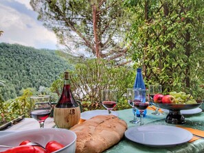 An outdoor dining setup with a table set for a meal, including bread, a bowl of tomatoes, and a bottle of red wine. - Country House With Swimming Pool and Garden With Mediterranean Plants (Bettona)