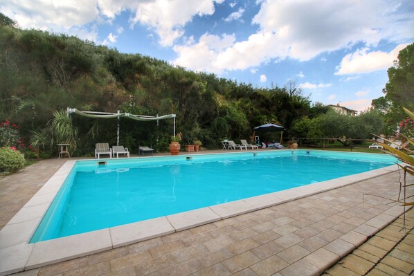 Une piscine rectangulaire bordée de carreaux, entourée d’un espace patio aménagé avec des chaises longues et des plantes en pot.