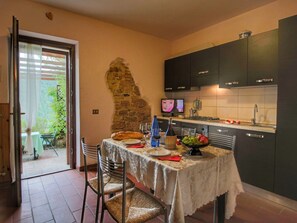 Une cuisine avec un mur en pierre, des meubles sombres et une table à manger dressée avec des assiettes, des verres et une bouteille.