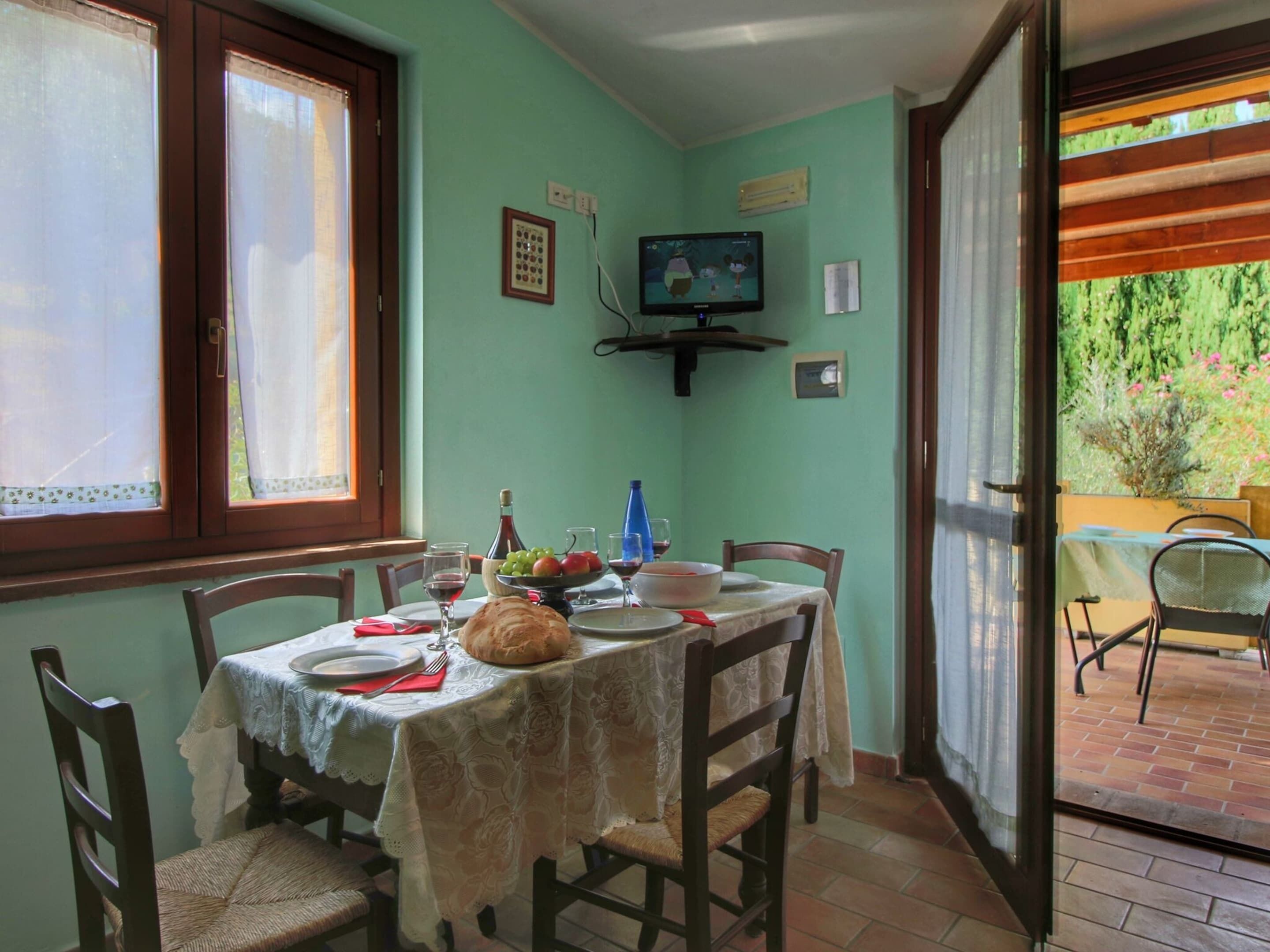 A dining area with a table set for four, a television mounted on the wall, and a window with curtains.