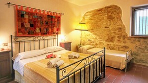 A bedroom with a bed, a nightstand, a lamp, a quilt, and a stone wall. - Country House With Swimming Pool and Garden With Mediterranean Plants (Bettona)