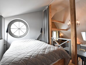 A bedroom with a large bed, a round window, a desk with a lamp, and a staircase. - Modern Holiday Home in Detershagen With Garden (Kroepelin)