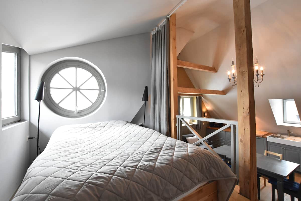 A bedroom with a large bed, a round window, a desk, and a staircase.