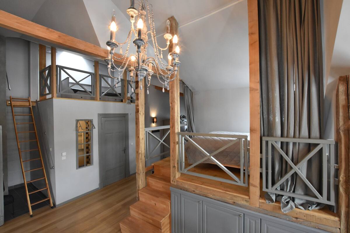 A loft-style bedroom with exposed wooden beams, a chandelier, and a loft bed.