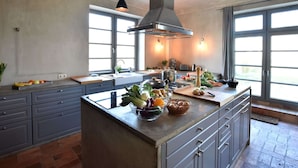 Une cuisine moderne dotée d’un îlot central, de grandes fenêtres et d’un plafond haut.