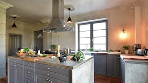 Une cuisine moderne dotée d’un grand îlot central, de meubles de couleur grise, d’une hotte en acier inoxydable et d’une fenêtre qui laisse entrer la lumière naturelle.