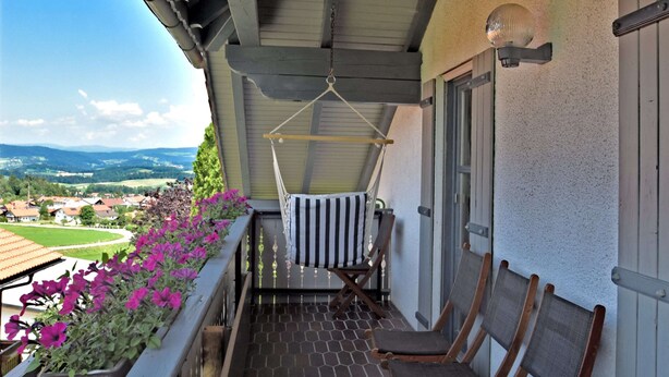 Ein Balkon mit Hängesessel, einem kleinen Tisch und einem Blumentopf mit violetten Blüten.