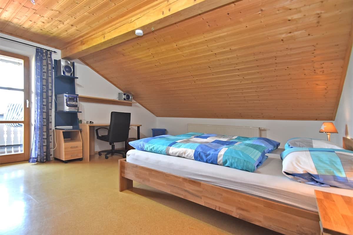 Une chambre avec un plafond en pente, un lit en bois, un bureau, une chaise et un radiateur.