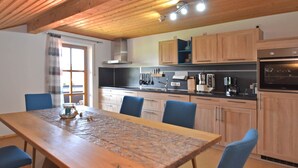 Eine moderne Küche mit Holzschränken, einem Esstisch mit blauen Stühlen und einem eingebauten Backofen.