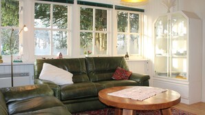 A cozy living room with a green leather sofa, a wooden coffee table, and a large window with a view of trees.