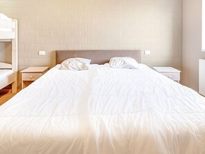 Een net opgemaakt bed met witte lakens in een kamer met een bakstenen muur en witte meubels.