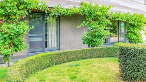 Un bâtiment moderne avec une façade en briques, de grandes fenêtres et un jardin bien entretenu, agrémenté de haies et de pelouse.