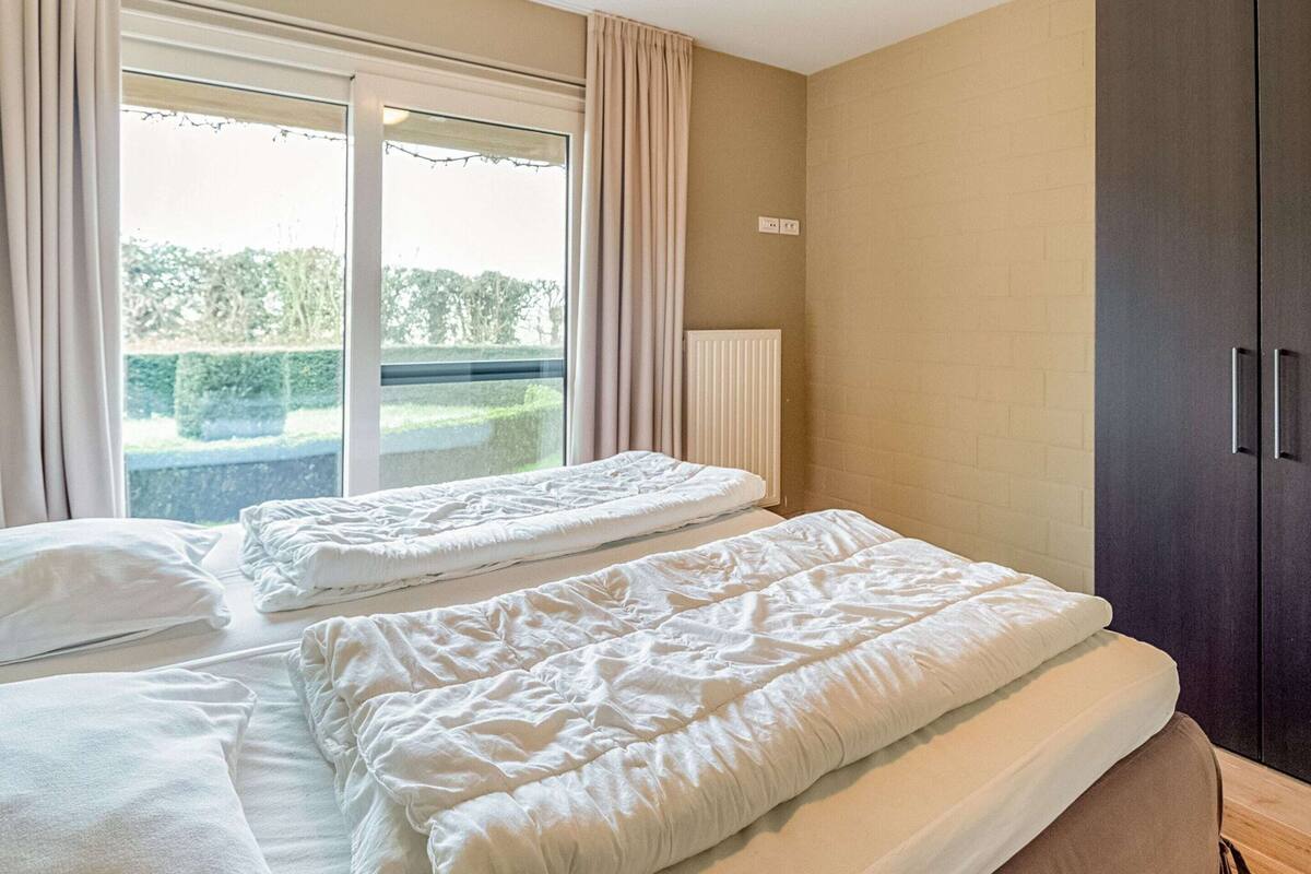 A bedroom with two beds, a window with curtains, a radiator, and a wardrobe.