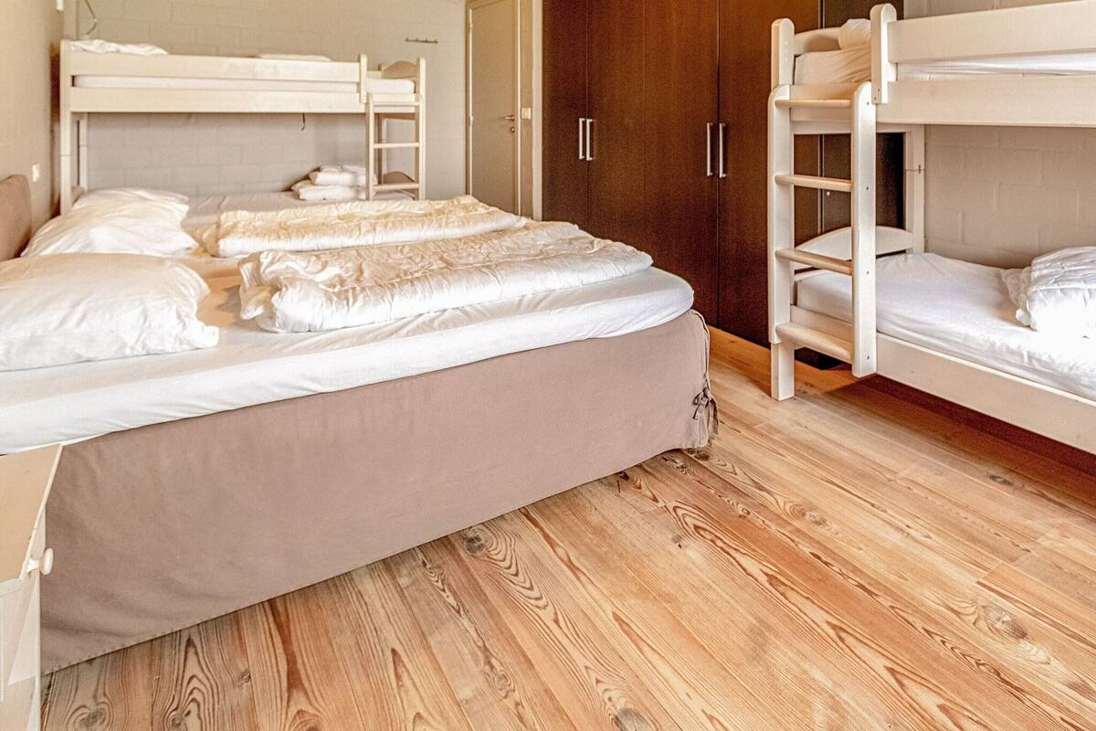 A dormitory room with bunk beds, wooden flooring, and a wardrobe.