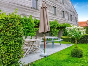 Een terras met een tafel en stoelen, een overdekte parasol en een strakke haag.
