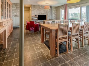 Een moderne keuken met een bakstenen muur, houten kastjes en een eethoek met een grote tafel en stoelen.