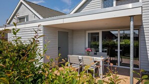 A modern house with a covered patio, a dining area with a table and chairs, and a garden with green foliage. - Charming Holiday Home in Zierow Near Seabeach (Zierow)