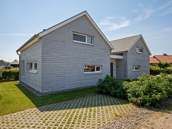 Une maison à deux étages, à l’extérieur gris, avec un petit porche à l’avant et une allée pavée.