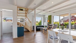 A modern interior with a wooden staircase, a dining area with white chairs, and large windows offering a view of the outside. - Charming Holiday Home in Zierow Near Seabeach (Zierow)