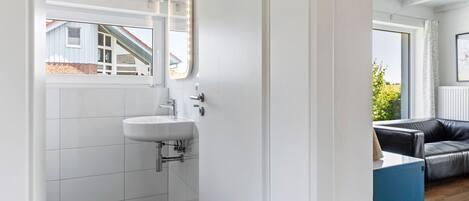 A modern bathroom with a white sink, a mirror with lights, and a view of a house through a window.