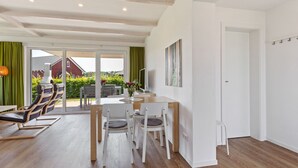 A spacious living area with a wooden floor, a dining table with chairs, a sofa, and a TV. There is a door leading to an outdoor area with a view of a red building and greenery. - Charming Holiday Home in Zierow Near Seabeach (Zierow)